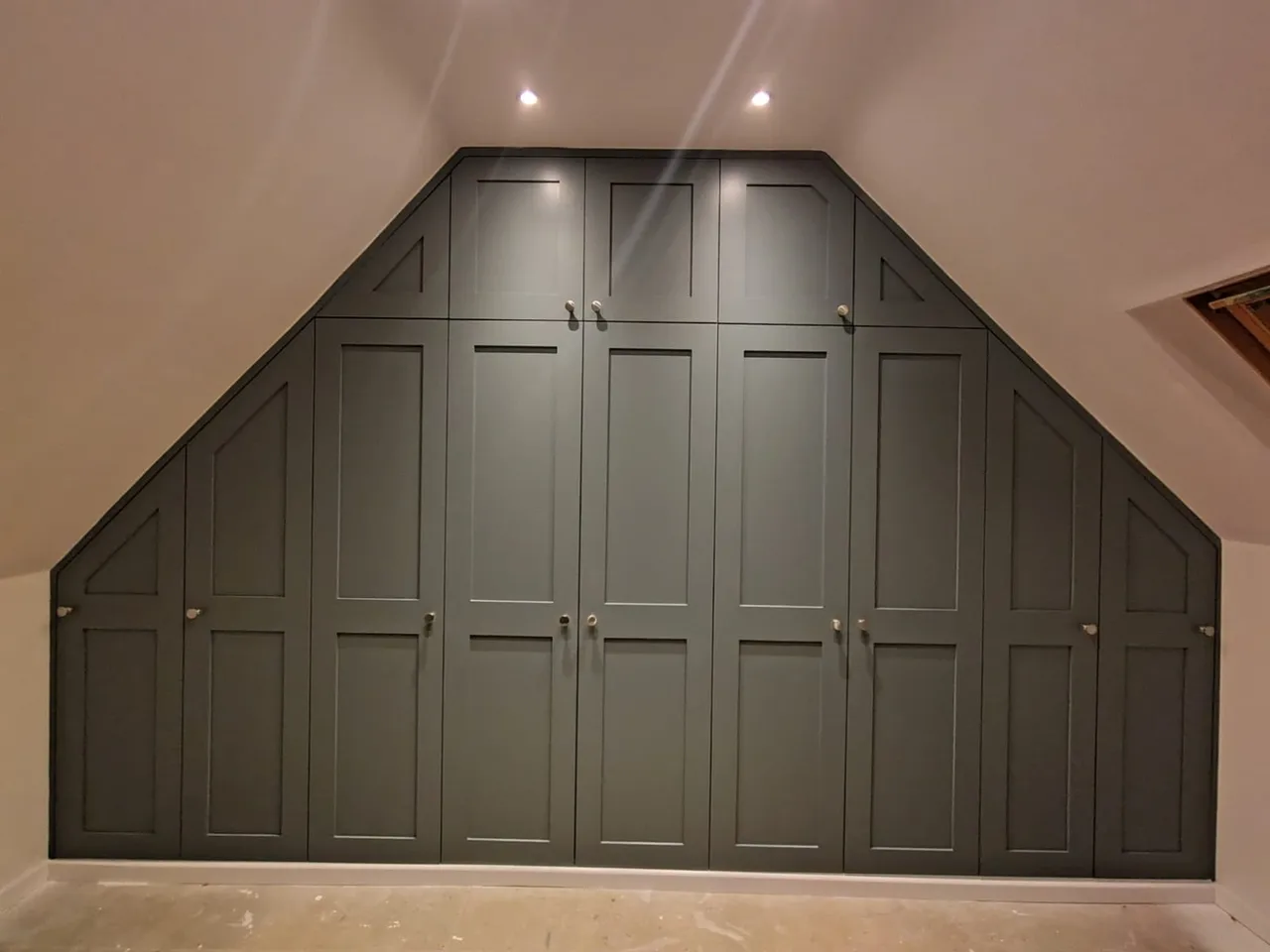 Bespoke fitted wardrobe with grey shaker-style doors and sloped ceiling design